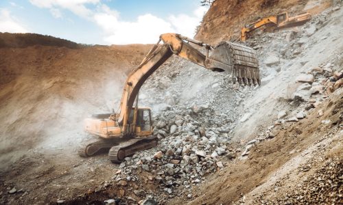 Industrial heavy duty excavator moving gravel on highway construction site. Multiple industrial machinery on construction site
